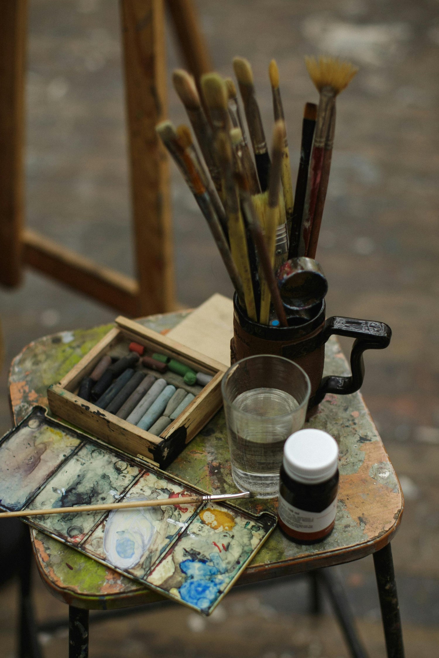 Paintbrushes in cup, next to paints and easel.