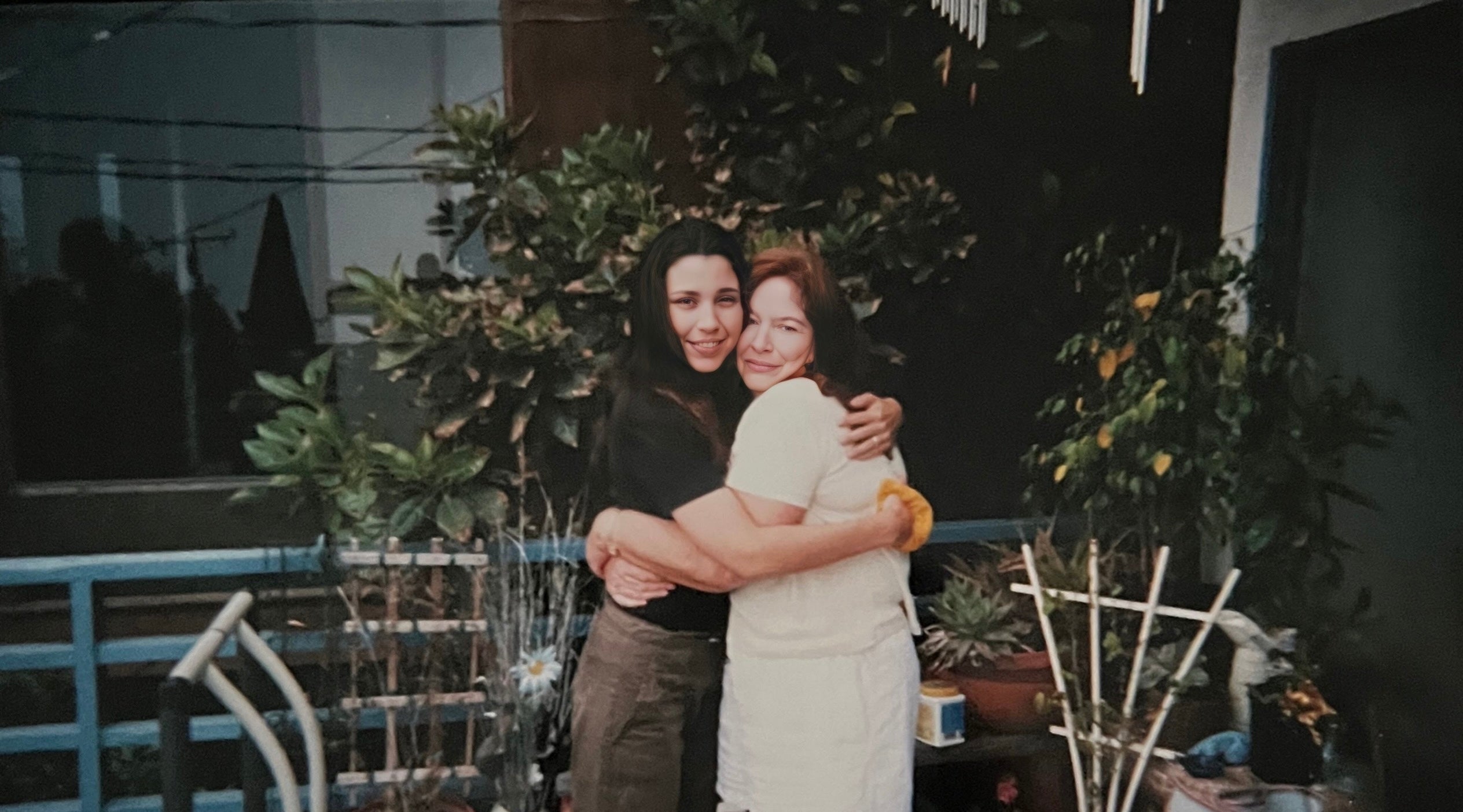Artist and her mother embracing lovingly in front of plants.